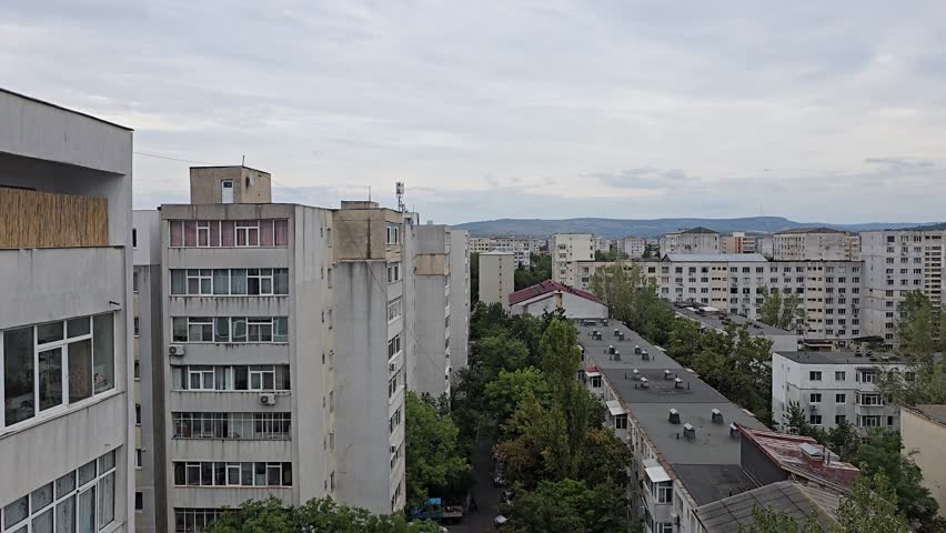 Panoramic view of residential communist-era apartment blocks in Iasi, Romania, under a cloudy sky. Urban cityscape featuring socialist architecture, green trees, and distant hills in Moldavia.