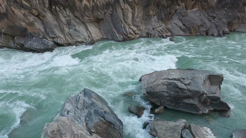 Powerful turquoise rapids surge between massive rocks in Tiger Leaping Gorge, showcasing the raw force of the Yangtze River cutting through a steep mountain canyon.