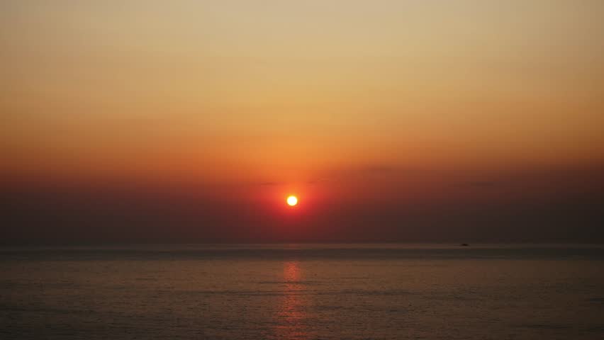 Sunset over the sea in Mani, Greece, with the red sun touching the horizon and warm orange tones in the sky, creating a calm and minimalist Mediterranean seascape.