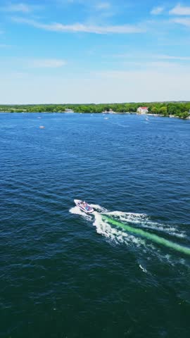 An aerial drone shot captures a speedboat cruising across the deep blue waters of Lake Delavan on a bright, sunny day.