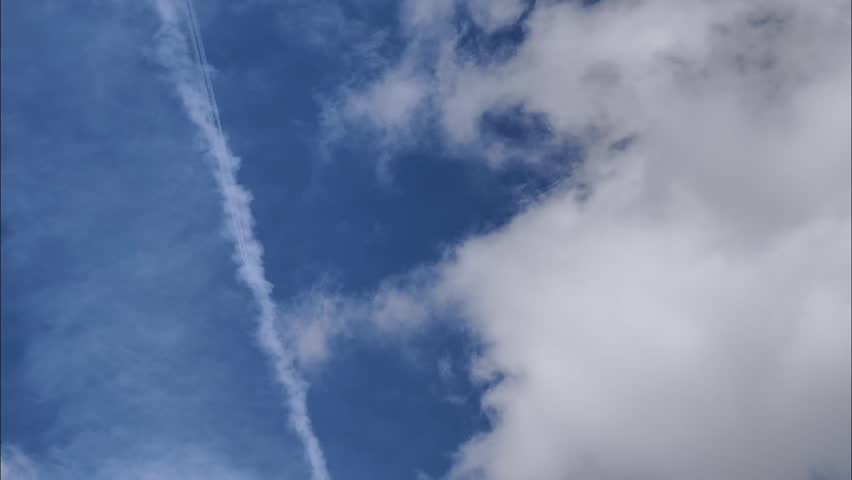 Low-angle video of a passenger airplane flying high in a blue sky with white condensation trails.