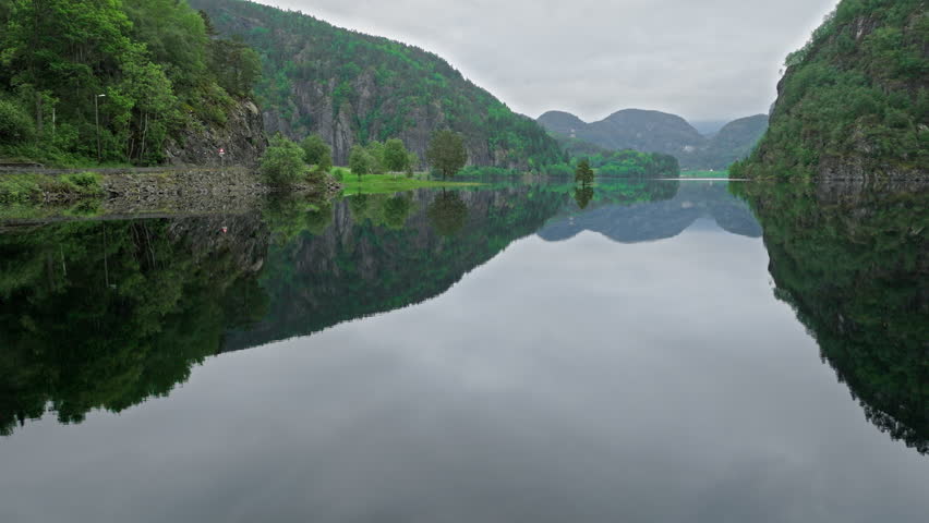Mirror-like lake surrounded by mountains and Norwegian houses in rural Norway. Serene tourist landscape with dramatic reflections, overcast light, and calm mood for outdoor exploration.