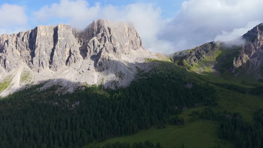 Majestic aerial view of the Dolomites mountains with clouds casting shadows over the green forest