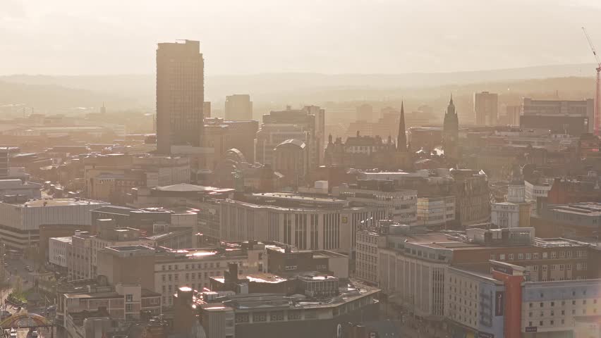 High aerial view of Sheffield urban landscape at dawn reveals distinctive city skyline with cathedral spire rising above commercial towers and Victorian industrial architecture, misty conditions