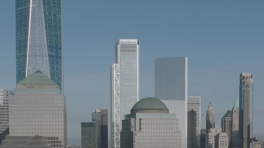 The skyline of New York City from an aerial viewpoint. Tall buildings shine in the sunlight against a blue sky. Busy city life is happening below.