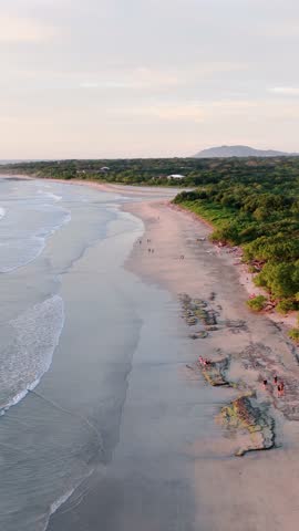 Aerial view of the beautiful shoreline of avellanas beach, costa rica. The ocean waves are gently washing ashore as people walk along the coast
