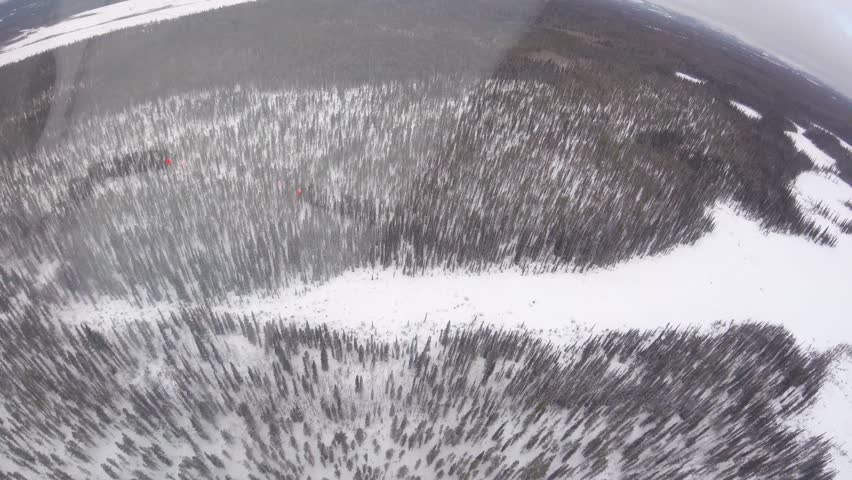 An expansive aerial view from a helicopter showcases the vast, snow-covered boreal forest and rugged terrain that defines the Yukon wilderness in winter