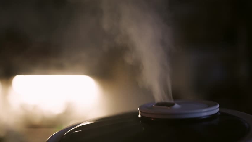 Ultrasonic modern air humidifier and aroma oil diffuser operating at home, releasing mist to improve air quality and create a relaxing atmosphere.