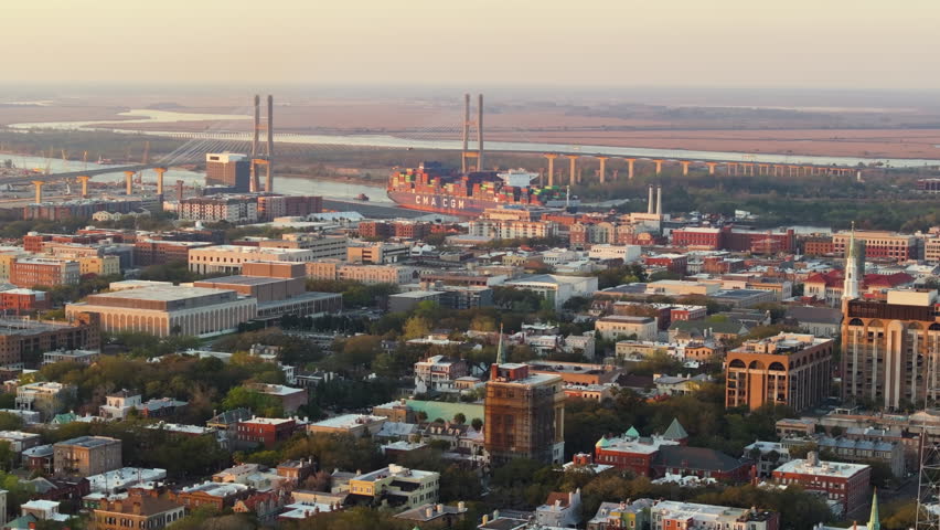 Savannah, Georgia. Container ship passing by old historic city center. View from above of illuminated streets at sunset. USA tourist attraction.
