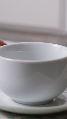 Vertical video. Fresh coffee pouring into white cup on table, cozy home breakfast and warm kitchen concept