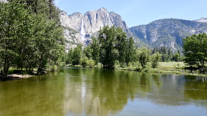 Mariposa County, California, USA - May 29, 2025: The Merced River slowly flows through Yosemite Valley as Yosemite Falls water tumbles to the valley floor in the background.