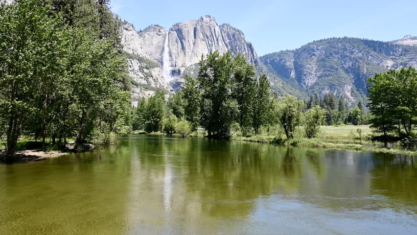 Mariposa County, California, USA - May 29, 2025: The Merced River slowly flows through Yosemite Valley as Yosemite Falls water tumbles to the valley floor in the background.