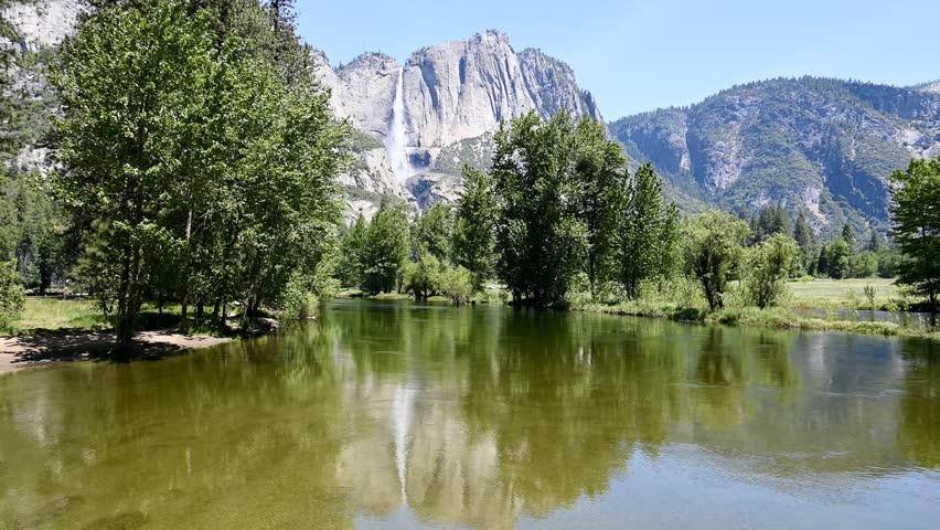 Mariposa County, California, USA - May 29, 2025: The Merced River slowly flows through Yosemite Valley as Yosemite Falls water tumbles to the valley floor in the background.