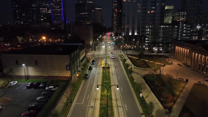 Aerial backwards shot over Charlotte, showing illuminated city streets, traffic and modern buildings. Vibrant urban atmosphere of major American city after dark. North Carolina, USA. Wide shot.