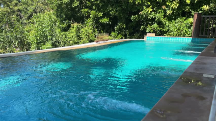 Private swimming pool at luxury villa on Koh Yao Yai island in Thailand featuring clear blue water, stone edge and lush tropical forest creating calm resort mood.