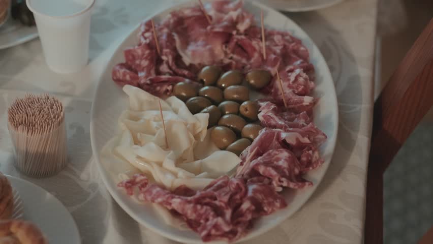 Oval plate arranged with sliced cured pork white cheese and green olives served for celebration