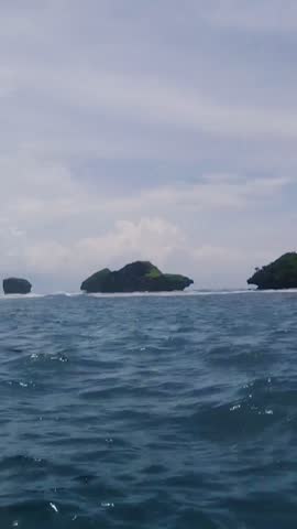 Beautiful landscape of small green rocky islands in the middle of the blue ocean under a bright cloudy sky in Indonesia