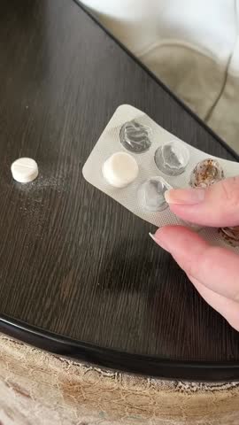 The woman pushes the pills from the blister onto the table. Dosage of tablets. Painkillers, antibiotics