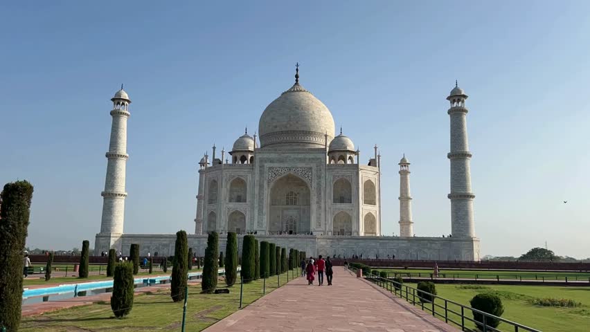 Captivating view of Taj Mahal reflecting morning light, showcasing intricate architecture. Tourists stroll leisurely along pathways, enjoying serene beauty of this iconic landmark.