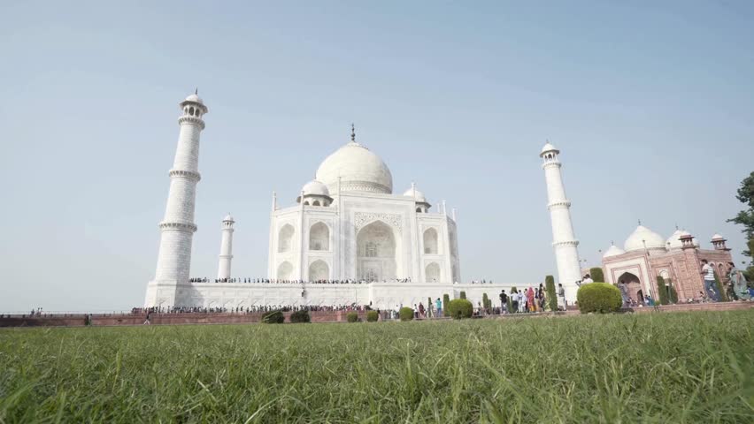 Imposing Taj Mahal stands proudly in Agra, showcasing intricate architecture. Visitors stroll around manicured gardens, capturing memories against a stunning backdrop.