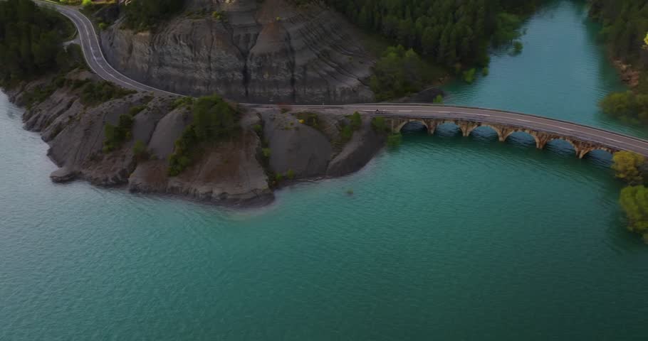 Drone tracking cyclists across arched road bridge over turquoise waters near Antiguo Balneario de Tiermas, Embalse de Yesa Reservoir, Aragon, on Camino de Santiago corridor area, Spain