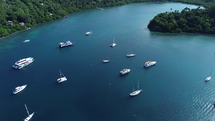 Aerial drone footage of small boats anchored in a calm tropical bay in Puerto Galera Philippines surrounded by dense green forest and clear turquoise water creating a peaceful travel and nature scene