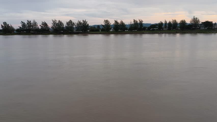 Peaceful wide river landscape at dusk with a line of trees on the far bank under a cloudy sunset sky. Calm water surface and serene nature view.