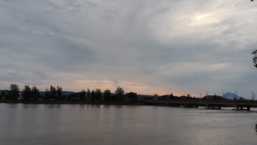 Peaceful wide river landscape at dusk with a line of trees on the far bank under a cloudy sunset sky. Calm water surface and serene nature view.