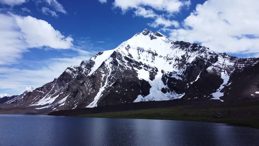 High-angle drone shot of a snowy mountain range against a dark sky. The camera looks down on the complex network of ridges and peaks, many of which are heavily covered in snow and ice. The contrast between the bright white snow and the dark, shadowed valleys creates a moody and dramatic aesthetic. This footage captures the raw power and inhospitable nature of high-altitude environments, highlighting the sheer mass of the earth
