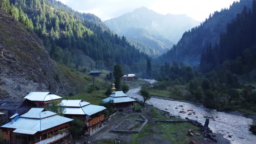 Aerial tracking shot of a mountain river through a deep canyon. The drone follows the rushing water as it carves through the steep rock walls. The perspective provides a sense of the power of natural erosion and the dramatic beauty of the high mountain environment.