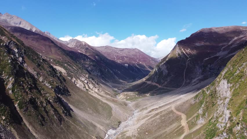 Aerial view of a mountain road winding through a high pass. The drone captures the intricate curves of the road as it navigates the difficult terrain. The surrounding peaks are rocky and barren, emphasizing the harsh conditions and the engineering feat of the highway.