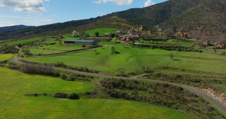 Aerial shot starts closer to hamlet of Ceresola in the municipality of Sabiñánigo, then slowly pulls back to reveal surrounding green meadows, and low Pyrenean foothills in northern Huesca