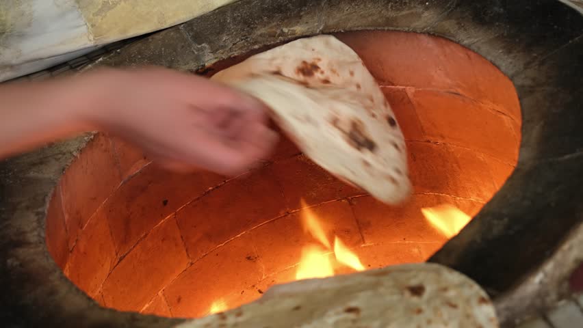 Traditional flatbread sticking to the walls of a hot tandoor oven for baking, a classic cooking method in a clay tandoor with flames visible, preparing fresh and delicious unleavened bread