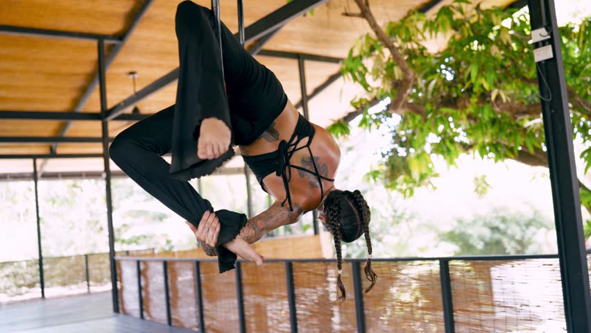 Strong and graceful woman with tattoos practicing aerial gymnastics. An acrobat performs complex elements hanging upside down on an aerial hoop
