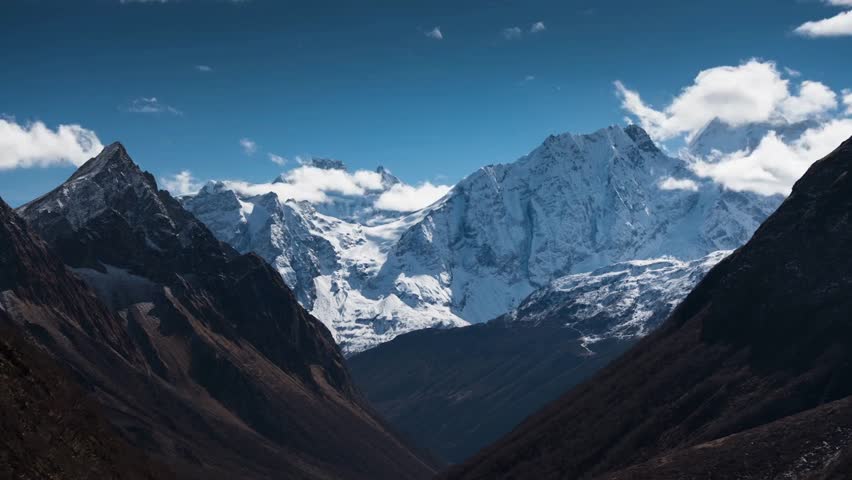 Expansive view of snow-capped Himalayan mountains surrounded by rocky terrain and dramatic clouds, showcasing the beauty of Nepal