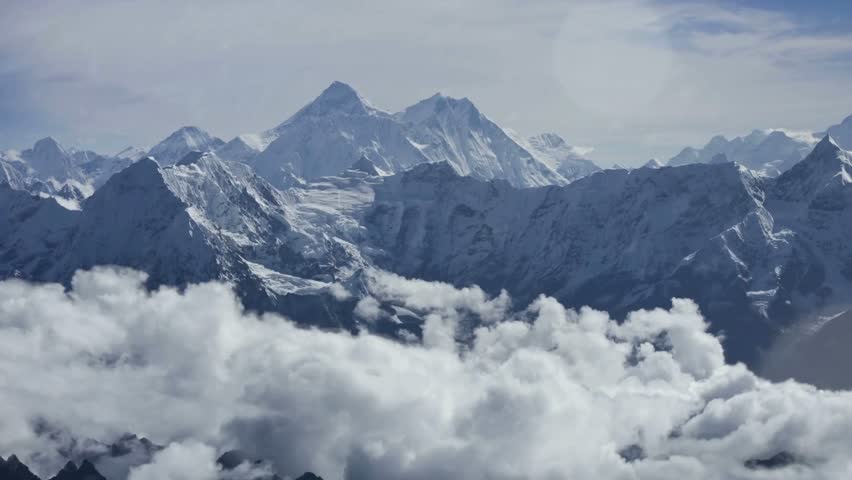 Stunning view of towering snow-capped mountains rising above a sea of clouds under a bright azure sky, showcasing the beauty of nature
