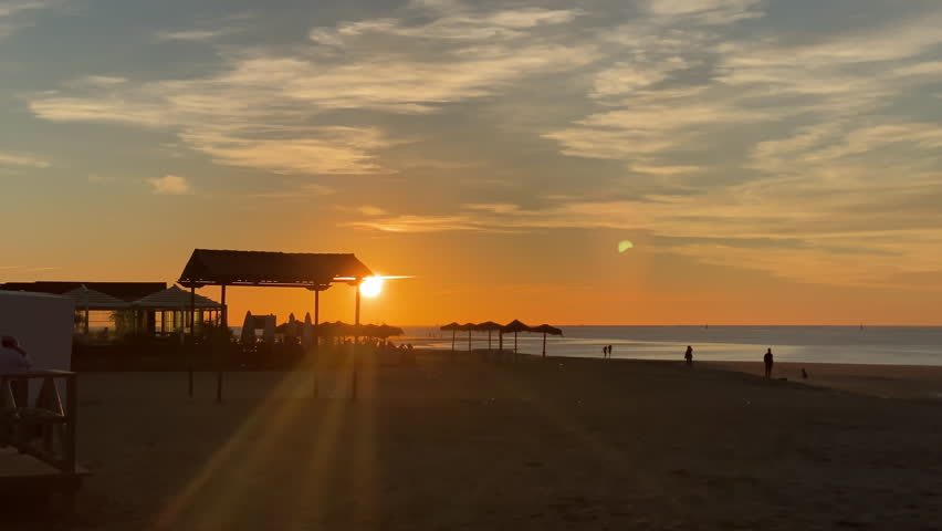 a Soft sunset light washes over the wide beach of Sanlucar de Barrameda as silhouettes walk along the low tide shoreline