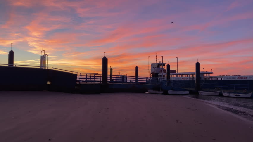 The Doñana ferry rests a low tide on the Sanlucar de Barrameda shore as fiery clouds paint the sky in vivid sunset colors