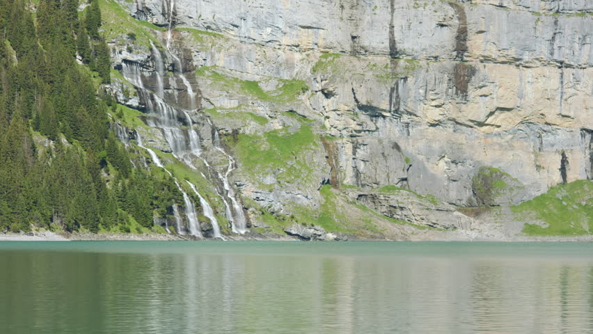 Mountain lake surface with a forested mountain and a waterfall visible in the background
