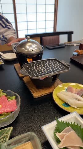 Person grilling fresh fish on a personal hibachi grill during a kaiseki meal