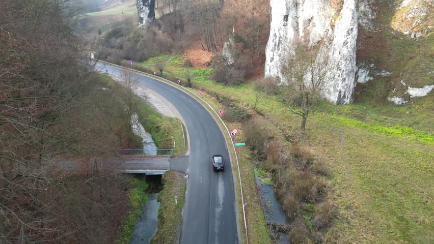 Aerial view of winding road through forested landscape, showcasing vehicles navigating curves. Auto riding at country route. Car trip. Surrounding nature and roadside elements, enhancing scenic beauty