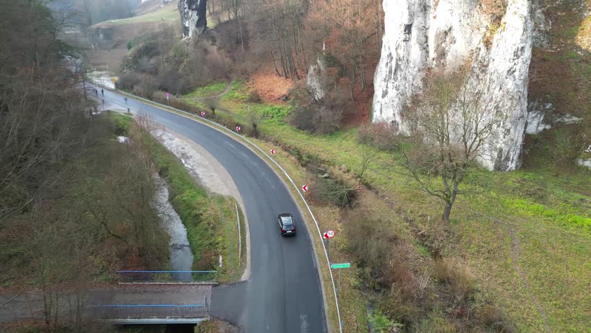 Aerial view of winding road through forested landscape, showcasing vehicles navigating curves. Auto riding at country route. Car trip. Surrounding nature and roadside elements, enhancing scenic beauty