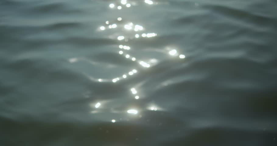 A close-up of water with bright sunlight reflections dancing on the surface. This shot captures the rhythmic motion and calm energy of a sea surface.