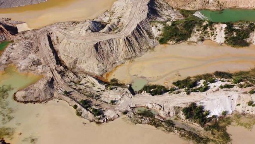 Waste clay and rock dumps and artificial lakes of different colored water in the ilmenite quarry, aerial view while moving sideways in summer sunny day
