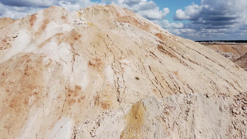Waste clay and rock dumps on the ilmenite quarry edge against the cloudy sky, aerial view close-up while moving sideways in summer sunny day
