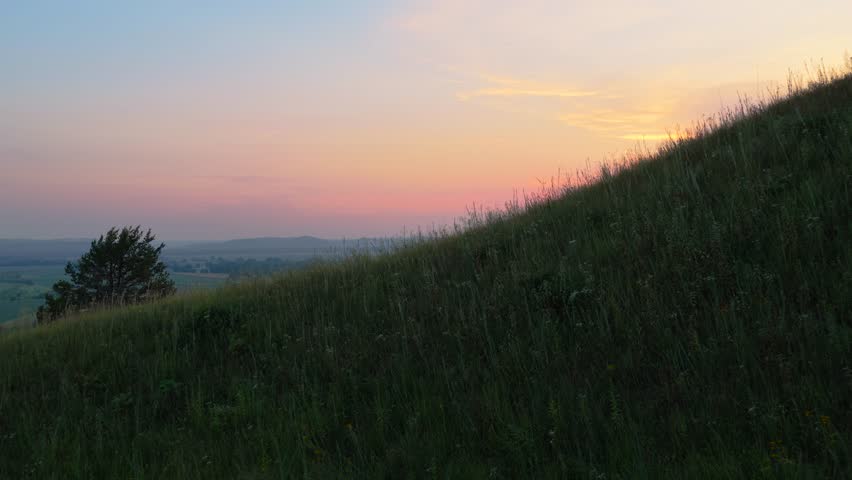 Drone footage flying toward a hill prairie at sunset, revealing river bluffs and expansive farmland below. Pink evening light bathes the floodplain, creating a scenic and cinematic rural landscape