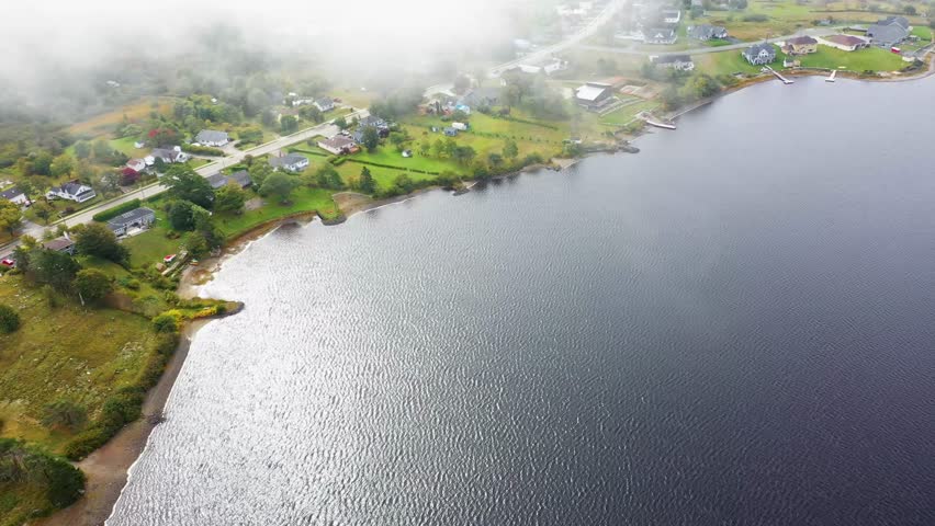 Aerial drone footage of the town of Yarmouth which is a port town in southwestern Nova Scotia, Canada showing a birds eye view of house and homes by the large lake going through clouds