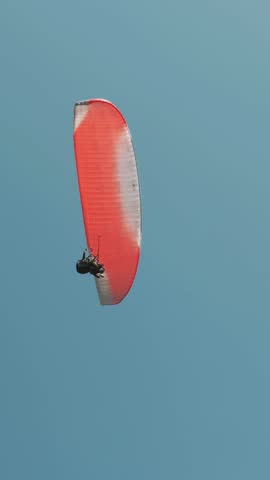 Flying red parachute against blue cleat sky. Tourist person glides with parachute over sea. Adventure activities. Vertical video