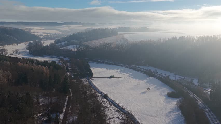 Winter landscape with railroad tracks. Forests and meadows covered with snow on a sunny day, viewed from a drone.