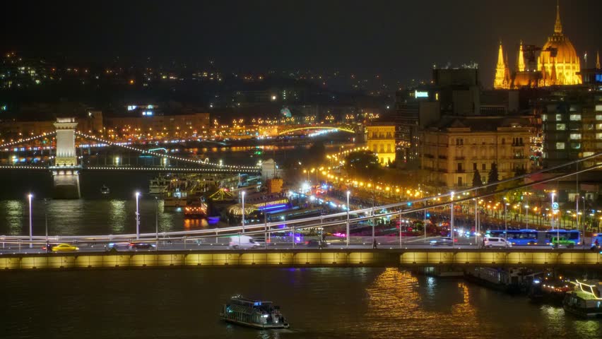 Panoramic view of Budapest city and Danube River at night, bridges, tour boats, urban architecture with beautiful illumination, street lights and road traffic